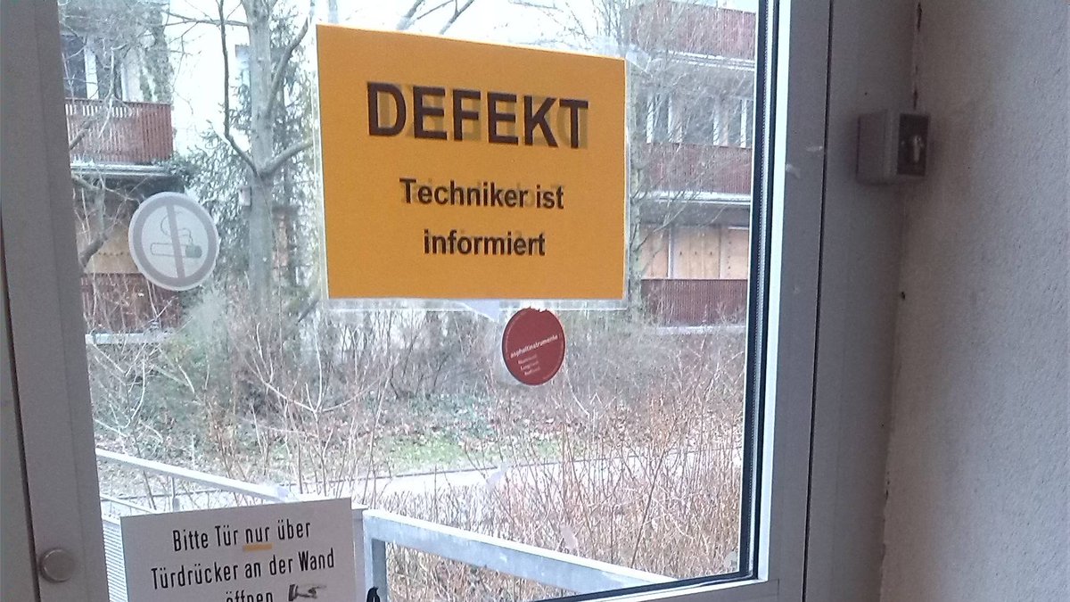 Eine Tür mit einer defekten Tür und einem aufgeklebten Schild: Defekt, Techniker ist informiert.